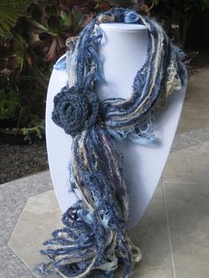 a blue scarf is hanging on a white mannequin with plants in the background