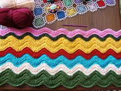 a crocheted blanket with yarn and balls of yarn on the table next to it