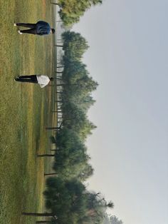 two people standing in the middle of a grassy field with trees and grass behind them