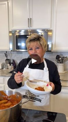 a woman holding a plate of food in front of a pot and pan on the stove