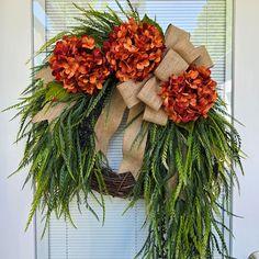 a wreath with orange flowers and greenery hanging on the front door's side