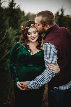 a pregnant couple cuddles in the woods for their portrait session at christmas tree farm