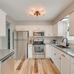 a kitchen with stainless steel appliances and white cabinetry, wood flooring, and hardwood floors