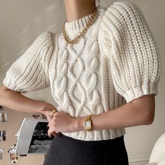 a woman in a white sweater and black skirt holding her hand on her hip while wearing a gold chain necklace