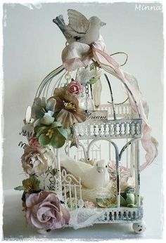 there is a bird in a cage with flowers on the top and an angel above it