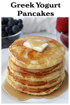 stack of pancakes with butter and syrup on white plate next to blueberries and strawberries