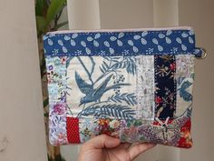 a hand holding up a patchwork purse with birds and flowers on the front side