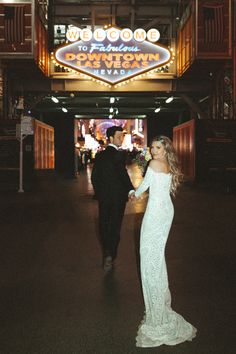 a bride and groom holding hands in front of the welcome to las vegas sign