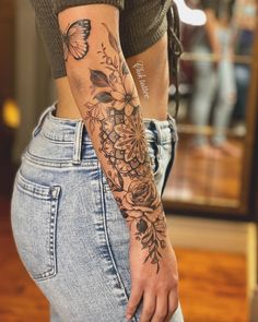 a woman's arm with flowers and butterflies tattooed on her left arm, in front of a mirror