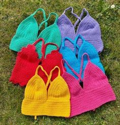 four crocheted swimsuits are laying on the grass, one is blue, one is pink and one is yellow