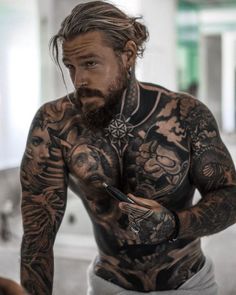 a man with tattoos on his chest and arm holding a cell phone in his hand