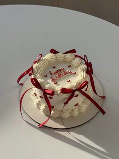 a white cake with red ribbon and happy birthday written on the top is sitting on a table