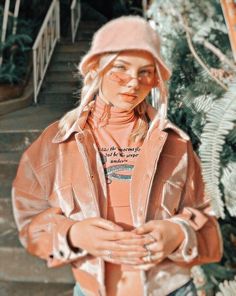 a young woman wearing a pink hat and jacket standing in front of some stairs with her hands on her chest