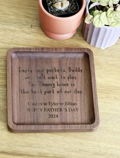 a wooden tray with a poem on it next to some potted plants and a planter