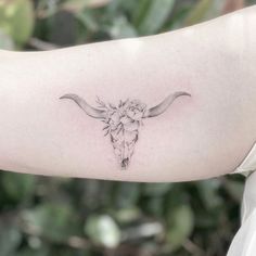 a woman's arm with a cow skull and flower tattoo on the left side