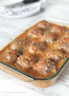 a casserole dish filled with meatballs and gravy on a marble counter