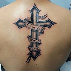 the back of a woman's shoulder with a cross and ribbon tattoo on it