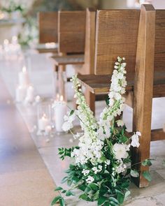 white flowers and greenery sit on the pews at a wedding ceremony with candles in the background