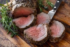 some meat is cut up on a cutting board with a knife next to it and garnished with herbs