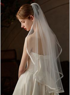 a woman in a wedding dress with a veil on her head, looking down at the floor