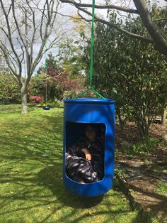 a child is sitting in a blue box on the grass near some trees and bushes