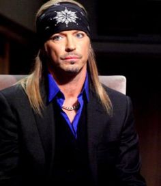 a man with long hair wearing a bandana and looking off to the side while sitting in a chair