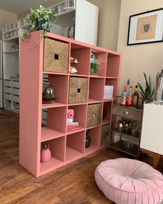 a pink bookcase with baskets on the top and bottom, in a living room