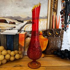 a red vase sitting on top of a wooden table next to books and other decorations