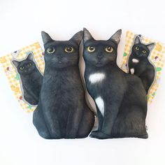 three black cats sitting next to each other on top of a white table with yellow checkered napkins