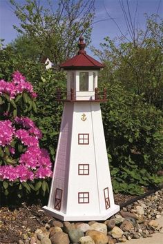 a white and red lighthouse sitting on top of a pile of rocks next to purple flowers