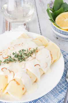 a white plate topped with ravioli covered in gravy and garnished with fresh herbs