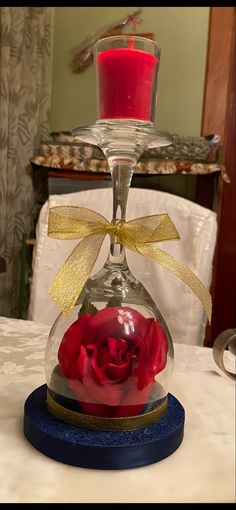 a red rose in a glass vase with a yellow ribbon around it on top of a table