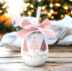 a cup with a pink bow and merry christmas trees on it sitting on a wooden table