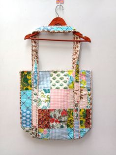 a multicolored patchwork bag hanging from a hook on a white wall with a wooden hanger