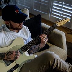 a man sitting on a couch with a guitar in his hand and wearing a hat