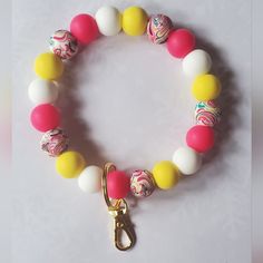 a bracelet with colorful beads and a gold charm on it's end, sitting on a white surface