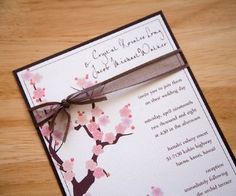 the wedding card is decorated with pink flowers and a brown ribbon on top of it