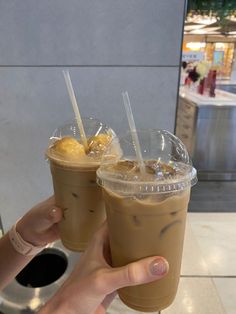 two drinks in plastic cups with straws and lemon wedges on the top, being held up by someone's hand