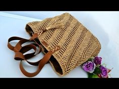 a straw bag sitting on top of a table next to purple flowers and a brown leather strap