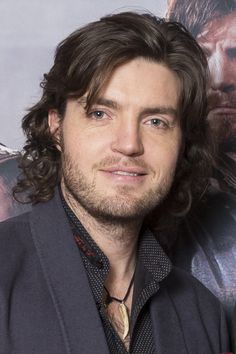 a man with long hair and blue eyes posing for a photo in front of a movie poster