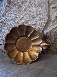 a metal flower dish sitting on top of a stone floor next to a rock wall