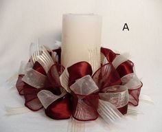 a white candle with red and silver ribbons around it on top of a table cloth