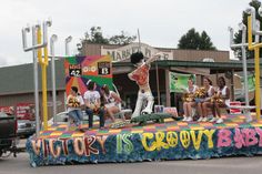 a group of people riding on the back of a float in a parade with cheerleaders