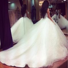 a woman in a white wedding dress looking at herself in the mirror with her back to the camera