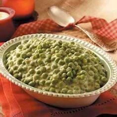 a white bowl filled with green peas on top of a red and white table cloth