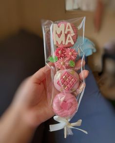 a person holding up a package of cookies with pink frosting and flowers on them