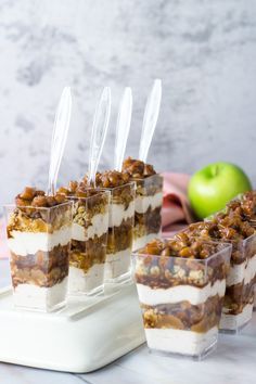 several desserts are arranged in individual cups on a tray with an apple behind them