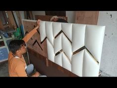 a man working on an art piece in his workshop with wood and white tiles behind him