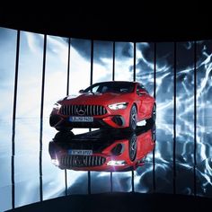 a red sports car on display in front of a large screen with blue and white lights