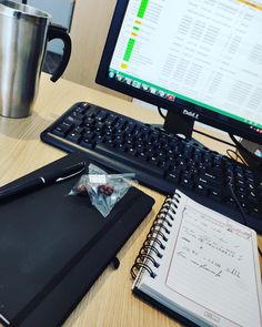 a desk with a keyboard, notebook and coffee mug on it next to a computer monitor